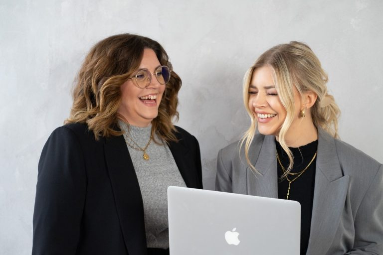 Louisa und Sabrina von getSocial schauen gemeinsam lachend auf einen Laptop und gehen die neuen Regeln zur KI-Kennzeichnung durch