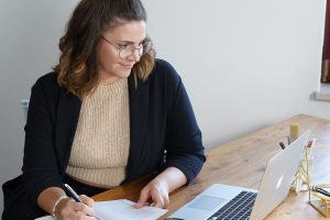 Eine der getSocial-Gründerinnen sitzt mit Laptop und Notizen am Holztisch und arbeitet an ihrem Content